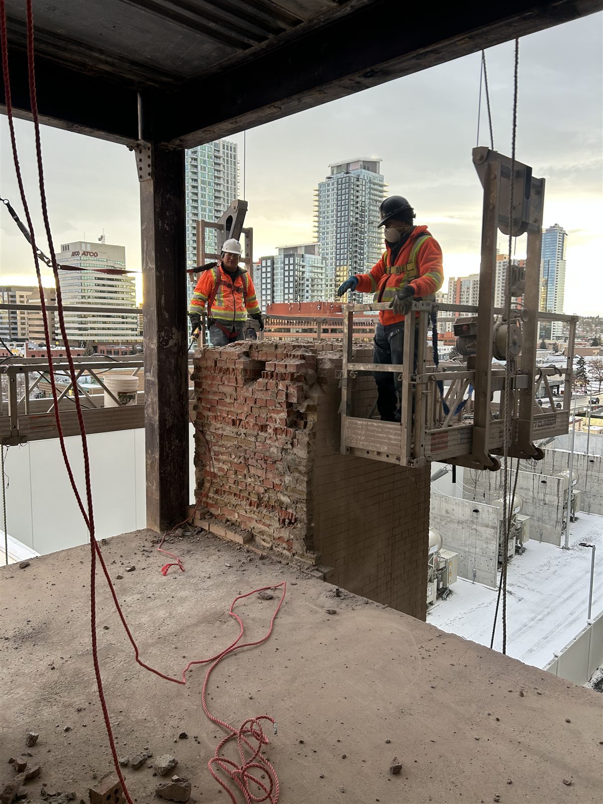 Labbe demolition crew working beside a partially demolished brick wall with Calgary buildings in the background
